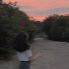 a blurry photo of a woman walking down a road at sunset with trees in the background