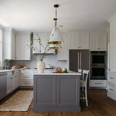 a large kitchen with white cabinets and gray island in the center, along with wooden flooring