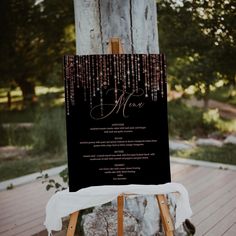 a wooden easel with a black and white wedding menu on it sitting in front of a tree