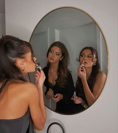 two women are standing in front of a mirror and one is brushing her teeth while the other looks at her reflection