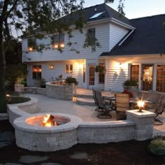 a fire pit in the middle of a patio with chairs around it and lights on