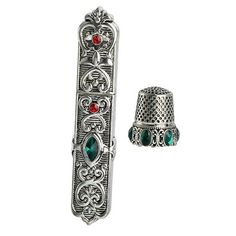 an ornate silver ring with red and green stones on the side, next to a bell