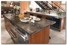 a large kitchen with an island and stainless steel appliances in front of the stairs that lead up to the second floor