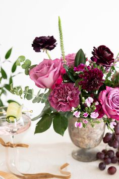 a vase filled with lots of purple flowers next to some grapes and other things on a table