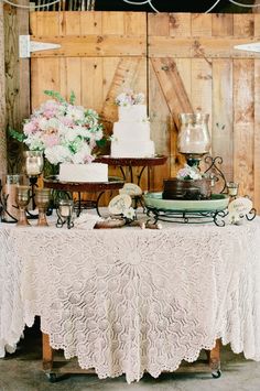 a table topped with a white cake and lots of flowers next to a wooden wall