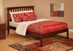 a bed with red and white comforter in a bedroom next to a rug on the floor