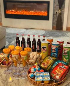 an assortment of snacks and drinks on a table in front of a fireplace with lit candles