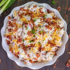 a bowl filled with cheese and bacon on top of a wooden table next to asparagus