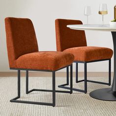 two orange chairs sitting next to each other on top of a carpeted floor in front of a white table