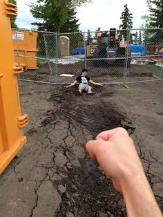 a person sitting on the ground in front of a fence with dirt and mud all over it