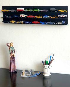 a black desk topped with a shelf filled with toy cars next to a white wall