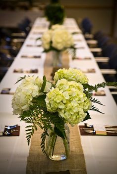 the table is set with white flowers in vases and place cards on each side