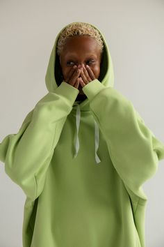 a young woman covers her face while wearing a green hoodie and covering her mouth with both hands