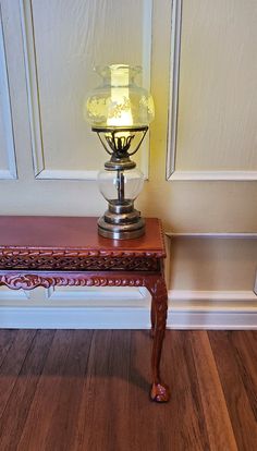 a lamp sitting on top of a wooden table next to a wall with white paneling