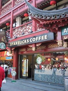 people are walking down the street in front of starbucks's coffee and tea shops