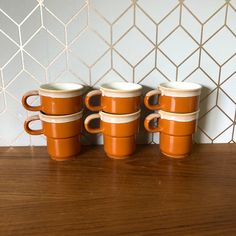 four orange coffee mugs sitting on top of a wooden table next to a white wall