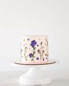 a white cake with purple and pink flowers painted on the top is sitting on a pedestal