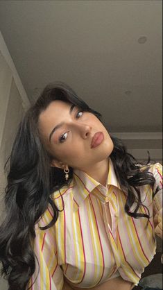 a woman with long black hair wearing a yellow and red striped shirt is posing for the camera