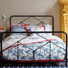 a bed with blue, white and red comforter on it next to a lamp