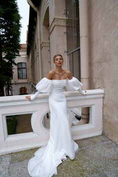 a woman in a white wedding dress leaning against a wall with her arms on the railing