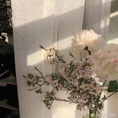 some white flowers are in a glass vase on a window sill with sheer curtains