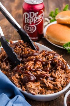 pulled pork with bbq sauce in a white bowl on a wooden table next to buns