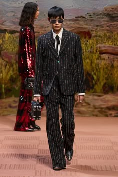 a man in a suit and tie walks down the runway with two other people behind him