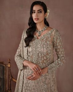 a beautiful woman in a beige outfit with jewelry on her neck and hands behind her back