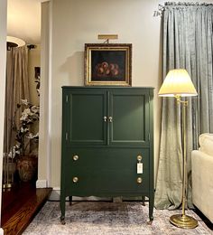 a green cabinet sitting in the corner of a room next to a lamp and couch