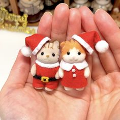 two small stuffed animals are in the palm of someone's hand, wearing red and white outfits