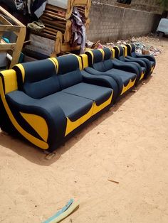 a row of black and yellow couches sitting on top of a dirt field next to a building