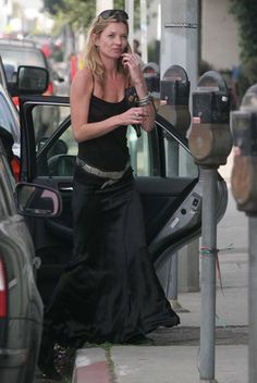 a woman in a long black dress getting out of a car with her hand on the door