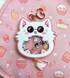 a white cat keychain on top of a pink bag with lots of charms