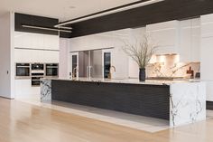 a large kitchen with marble counter tops and white cabinets, along with hardwood flooring