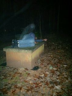 a man laying on top of a cement bench in the middle of a forest at night