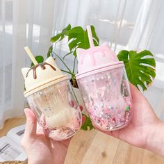 two pink cups with straws in them are being held by someone's hand