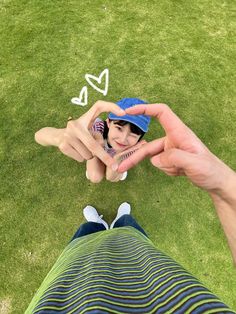 two people holding hands in the grass with hearts drawn on them and one person wearing a hat