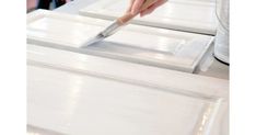 someone using a brush to paint the top of a white cabinet door with glass inserts