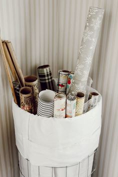 a white basket filled with lots of different types of wrapping paper on top of a wall