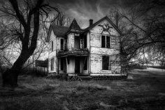 an old abandoned house in the middle of a field with trees and grass around it