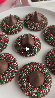 chocolate covered pretzels with sprinkles on a white plate next to red and green candies