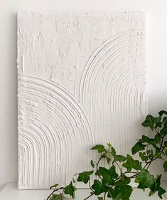 a potted plant sitting on top of a table next to a white wall art piece