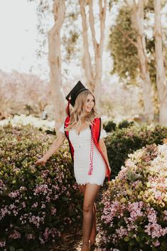 a woman in a graduation cap and gown walking through some bushes with her hand on her hip