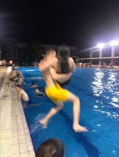 a man jumping into a swimming pool with people watching from the sidelines at night