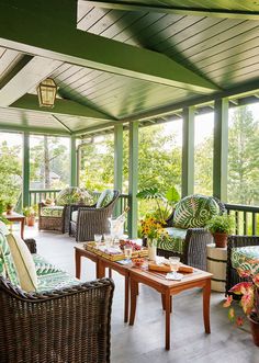 a covered porch with wicker furniture and potted plants on the table, in front of large windows