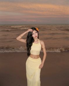 a woman standing on top of a sandy beach next to the ocean wearing a yellow skirt