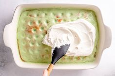 a hand holding a spoon over a bowl of green pudding with whipped cream on top