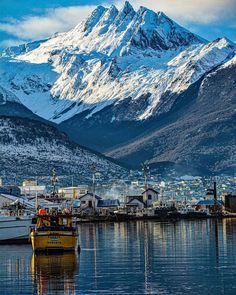 boats are docked in the water with snow covered mountains in the background