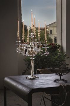 a dining room table with many candles on it in front of an open window and potted plant