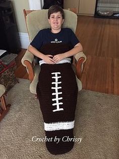 a young boy sitting in a chair with a crocheted football blanket on it